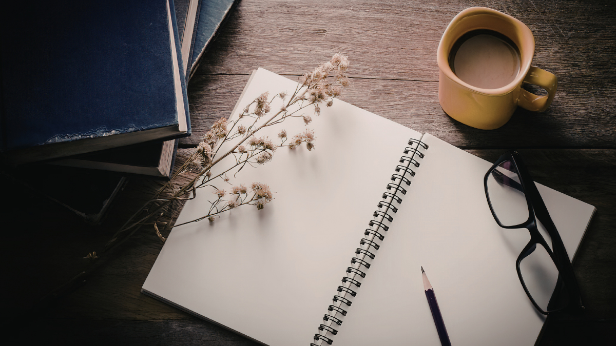 Blank notebook with glasses, pencil, flowers, and coffee on a wooden table