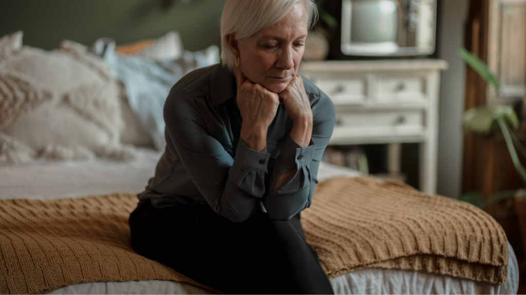 Woman sitting on bed looking tired and thoughtful