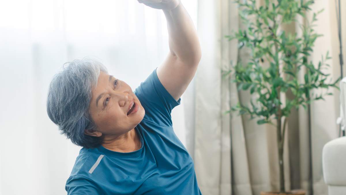 Woman in a blue top doing a gentle seated stretch at home near a window
