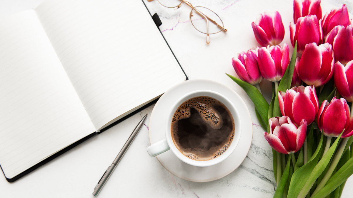 Open notebook with coffee and pink tulips on a white table
