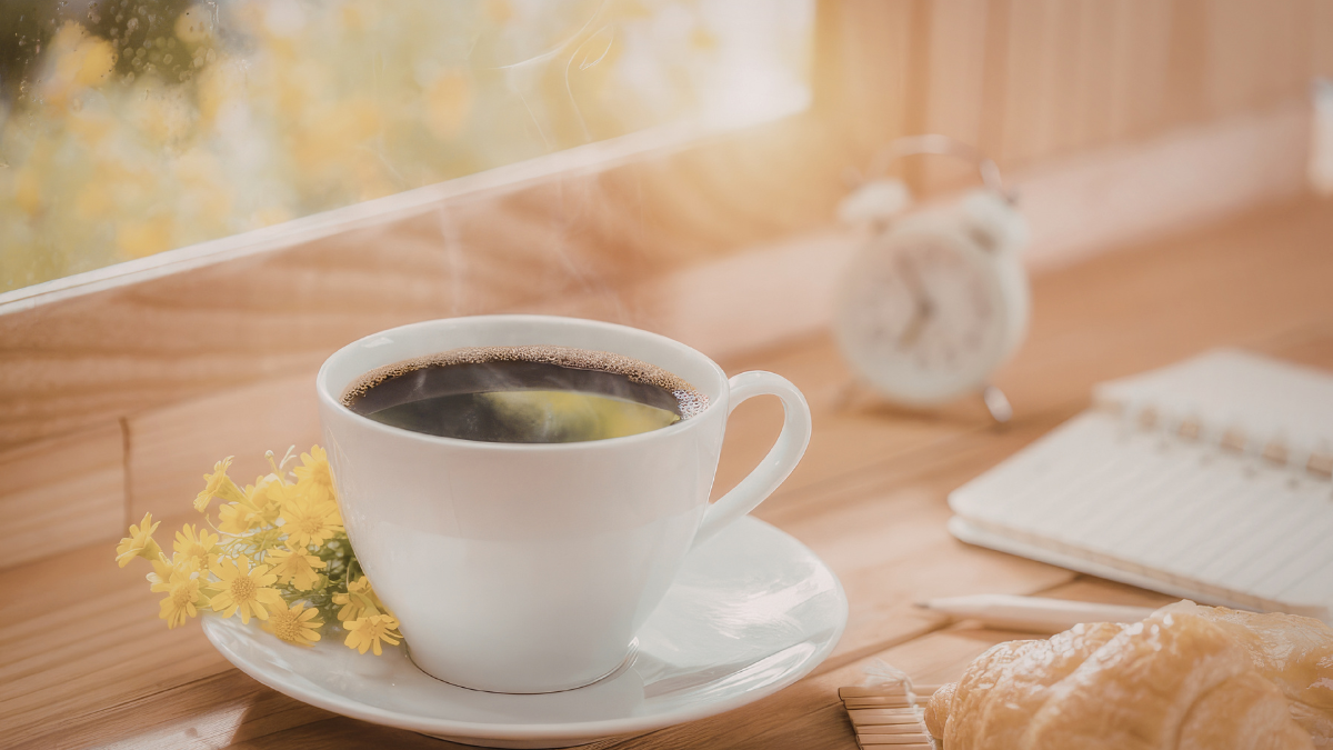 Cup of coffee by a sunny window with a notebook and clock in the background
