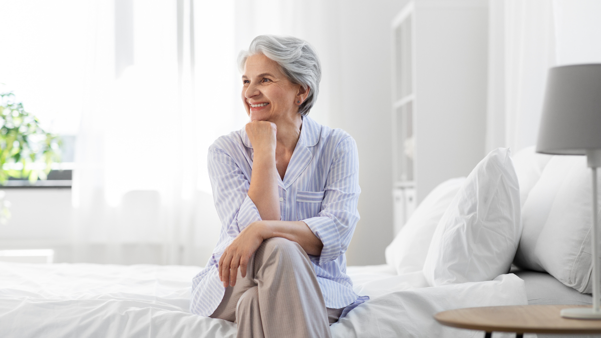 Woman sitting on the bed in soft morning light, beginning the day with gentle wellness habits for low energy.