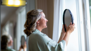 Woman holding a mirror near a window with soft natural light.